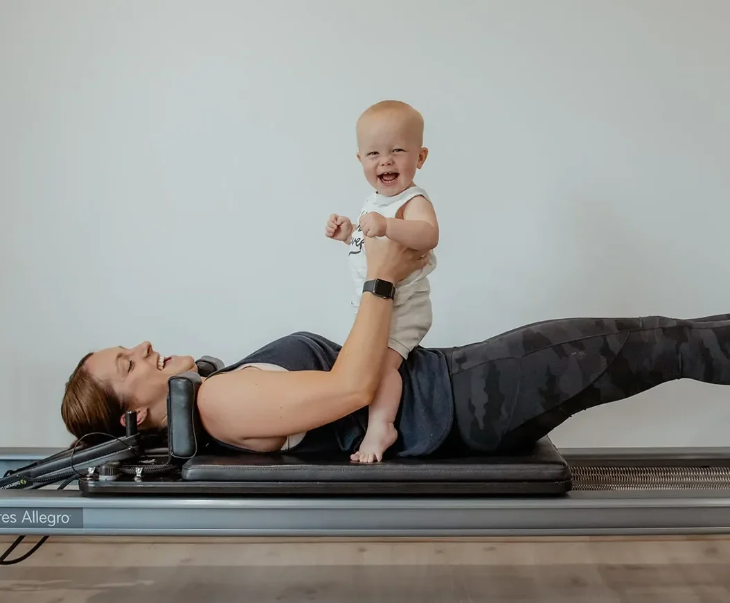 Mom holding her baby while doing exercises in a postnatal Pilates reformer class