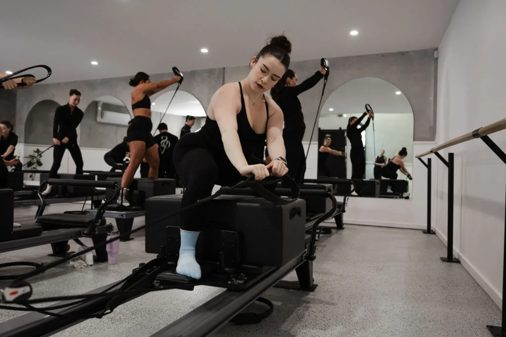 Reformer pilates instructor pulling long straps while showing a core exercise on Pilates equipment