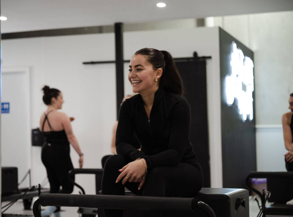 Renee Landcaster resting on a reformer Pilates machine with a smile during a cooldown
