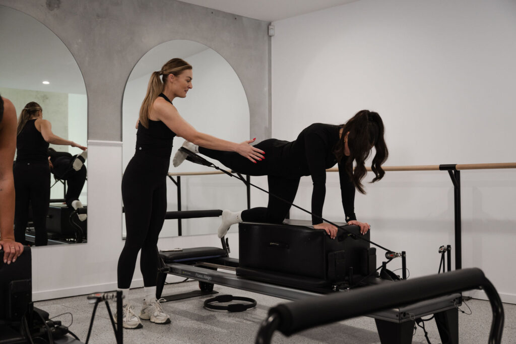 Alyce guiding a girl to maintain proper form on a Pilates reformer