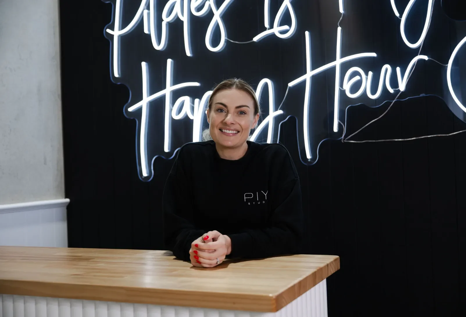Alyce Doran standing and smiling warmly at the front desk of PIYO Studios